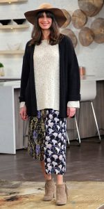 Woman model wearing black cardigan, white sweater, floral skirt and tan fringe boots